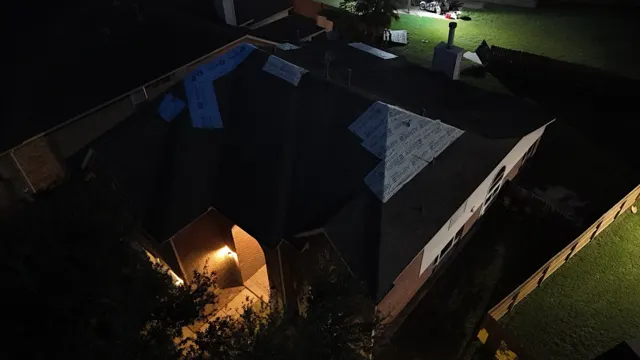 Night drone photo of a third Cypress home after the tornado, with underlayment patches sealing the damaged hip and ridge areas. Emergency tarping does not stop at sundown when rain is in the forecast, so the crew kept working into the night to make sure this family's roof was sealed before the next storm.