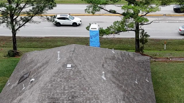 Drone photo of the Cypress home after the emergency dry-in, with the blue-wrapped chimney chase standing above the hip roof. Broken fence panels and downed limbs still line the property along the road, showing how hard the tornado hit. From above, the roof vents, skylight and shingle field can also be checked for wind and debris damage as part of the full storm inspection.