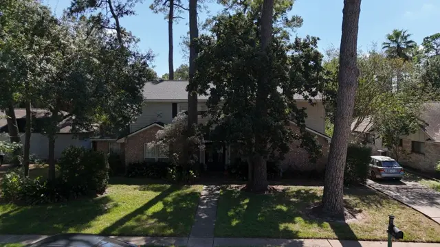 Street view of the Cypress home after the roof replacement, framed by mature pines and oak trees. Homes under heavy canopy like this are common in Cypress, and they need roofs installed to handle constant needle and leaf debris. The new roof restores curb appeal and gives the homeowner a roof they can insure.