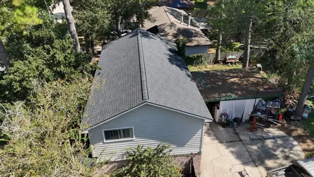 The completed full roof replacement on the Cypress home, seen from the drone. New dark gray architectural-style shingles and a fresh ridge cap cover the entire roof, with clean lines down each slope. A new roof like this brings an older home back into compliance with what insurance companies look for, so the homeowner can get coverage again.