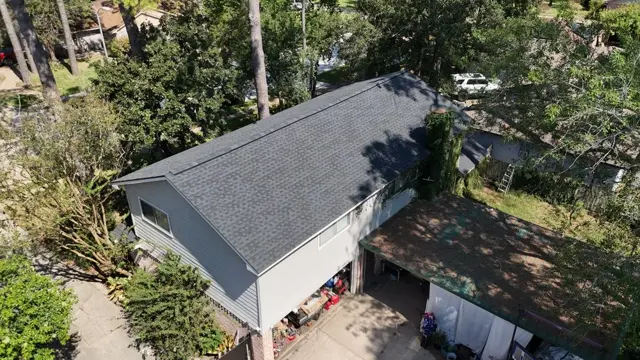 Another aerial angle of the finished roof over the garage side of the home, with straight shingle courses, new ridge cap and the yard cleaned up after the tear-off. For homeowners paying cash, a clear photo record of the finished work is also useful proof of the roof's age and condition when shopping for a new insurance policy.