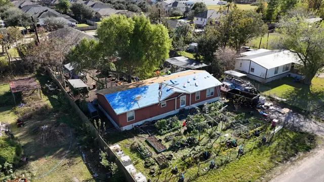 Drone photo of the whole property during the roof replacement in Pearland, Texas, with blue synthetic underlayment covering the roof, garden beds in the backyard and the surrounding neighborhood. Aerial photos show the full scope of a roofing project at a glance and give homeowners a view of their roof they never get from the ground. Cloud IX uses drone photography on inspections and builds to document every slope.