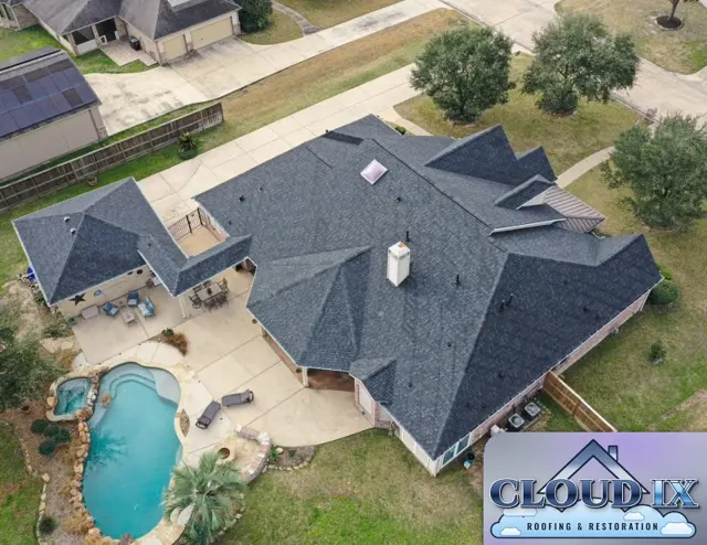 Rear aerial view of the completed roof over the main house and the separate hip roof covering the outdoor living area beside the pool and spa. Complex roofs with many hips and valleys take more cutting, more ridge cap and more careful flashing work, and every one of those transitions is a place a lesser install can leak. The dark charcoal shingles give the brick home a sharp, uniform look from every side.