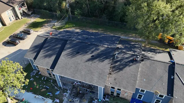 Drone view of the final sections of new shingles on the apartment building, with installers finishing ridge details and the old, damaged section at one end ready to be torn off and replaced. A new roof across the whole complex gives the property manager one uniform roof system, a fresh warranty period and fewer leak calls from residents.