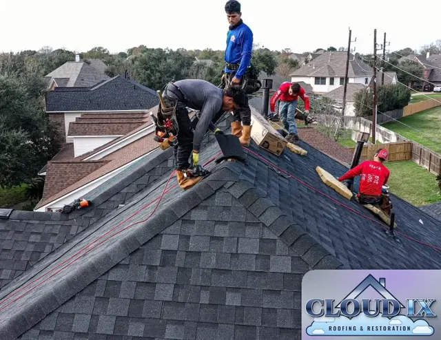 Four crew members finish the hip and ridge caps on the Tomball reroof, with nail guns, air lines and cap shingle boxes staged on the slope and the surrounding neighborhood behind them. A full crew working the caps at the same time keeps the job on schedule and gets the roof fully sealed in a single day.