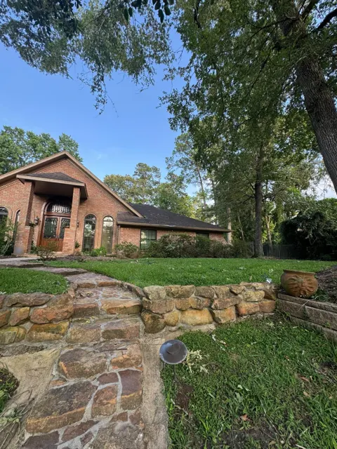 The same Tomball home after the tree clearing and cleanup: limbs removed from the roof and entry, debris hauled away and the lawn, walkway and stone retaining wall cleared. With the roof uncovered, the shingles and gutters can be inspected for impact damage and any needed repairs or an insurance claim can move forward. A clean property is also safer for the homeowner and makes the roof inspection faster and more accurate.