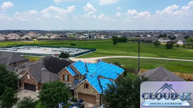 Wind storm repair in The Woodlands, Texas: the entire roof dried in with blue synthetic underlayment after the wind-damaged shingles were torn off. Drying in the full roof the same day protects the home if more weather moves in before the new shingles go on. Open fields and rows of newer homes stretch out behind the subdivision, the kind of exposed setting where high winds hit roofs hardest.